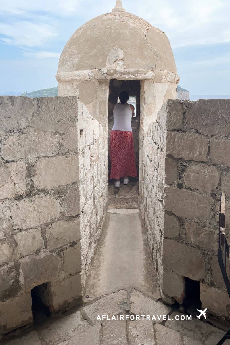 Woman standing inside a lookout tower on the Dubrovnik City Walls facing the sea
