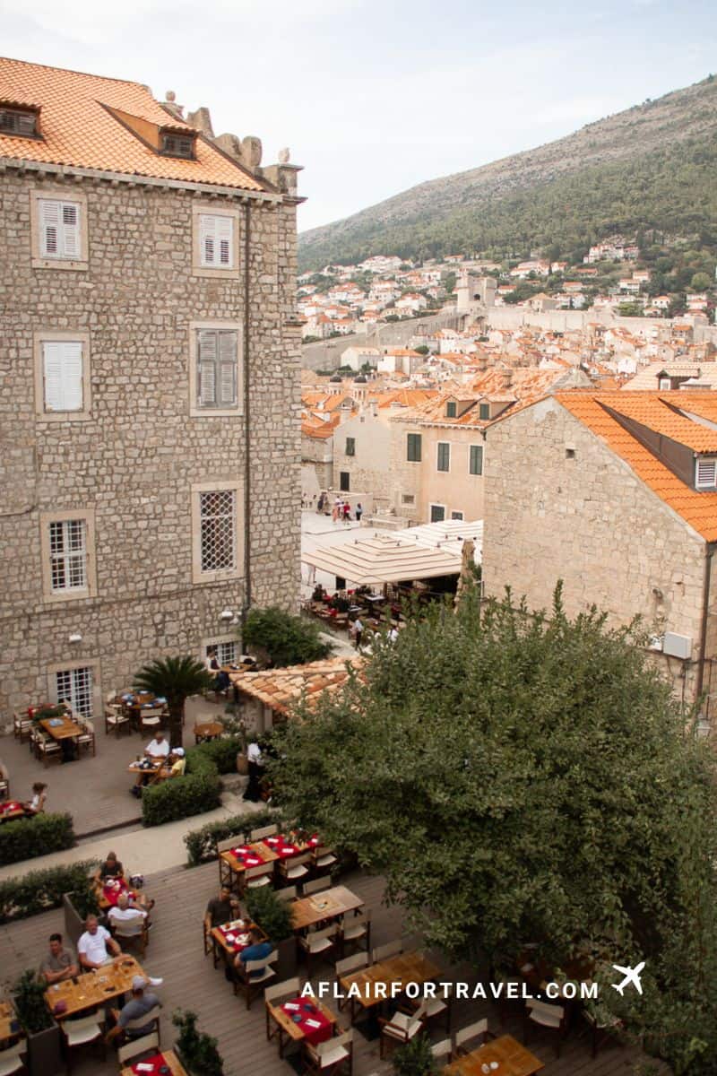 Aerial view of a bustling outdoor restaurant terrace at Rudjer Restaurant & Bar, surrounded by medieval stone buildings and trees.