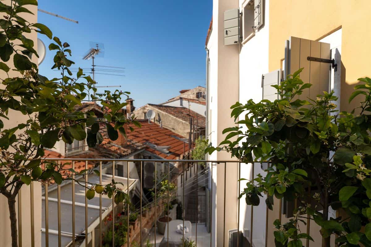 A balcony at Hotel Spirito Santo Palazzo Storico flanked by potted lemon trees, with views across the terracotta rooftops of the surrounding old town under a clear blue sky.