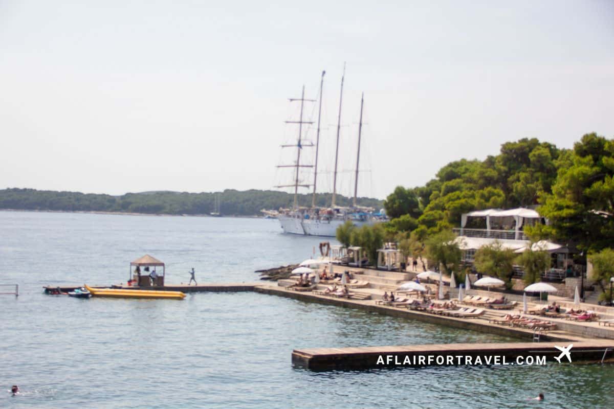 Luxury beach club on Hvar Island with sun loungers, umbrellas and a tall ship anchored in the bay, one of the top Croatia travel tips is that you shouldn't expect long, sandy beaches.