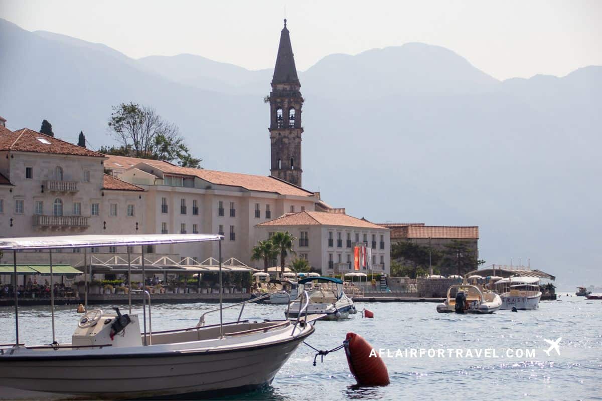 Boats moored in the bay at Perast Montenegro with a historic church bell tower and mountains in the background