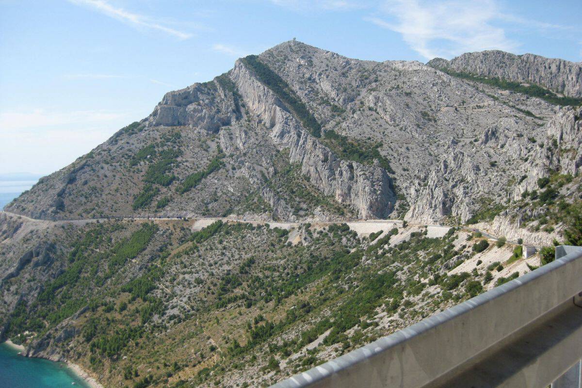 Narrow winding mountain road carved into dramatic rocky cliffs along the Croatian coast, a key Croatia travel tip is to understand that coastal driving can be slow