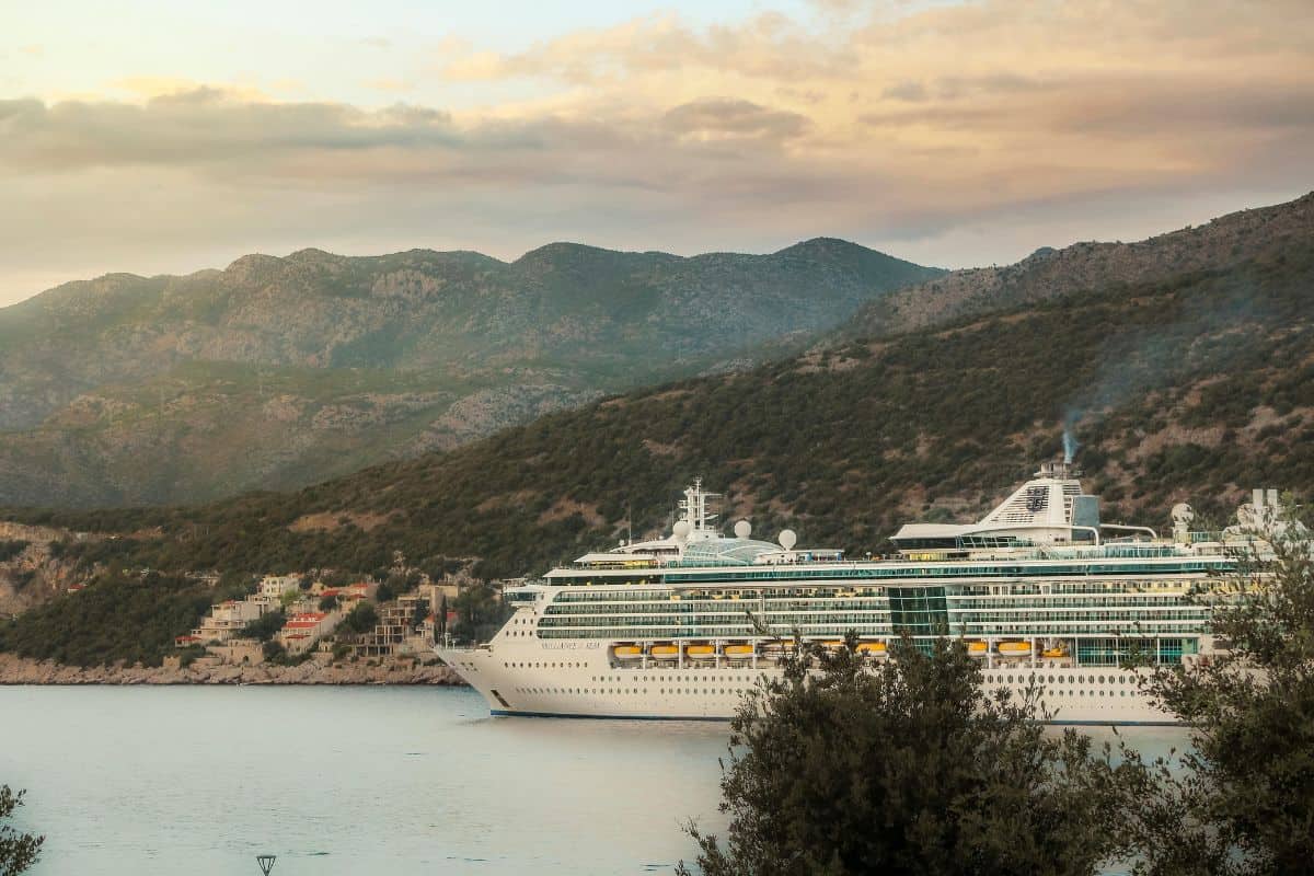 A large cruise ship docked in a Croatia port at sunset with mountain backdrop; checking cruise ship schedules in advance is one of the most important Croatia travel tips for avoiding crowds in popular destinations