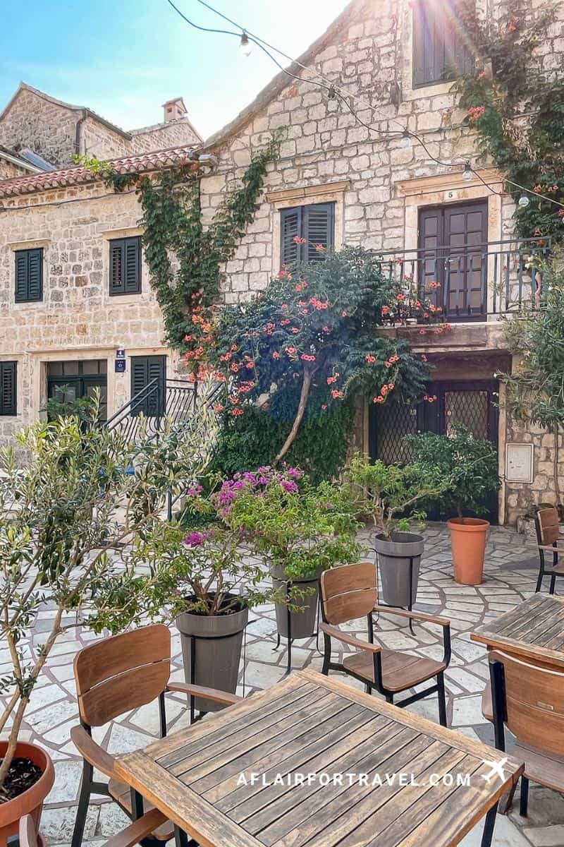 A charming flower-filled stone courtyard café in Croatia with wooden tables and string lights