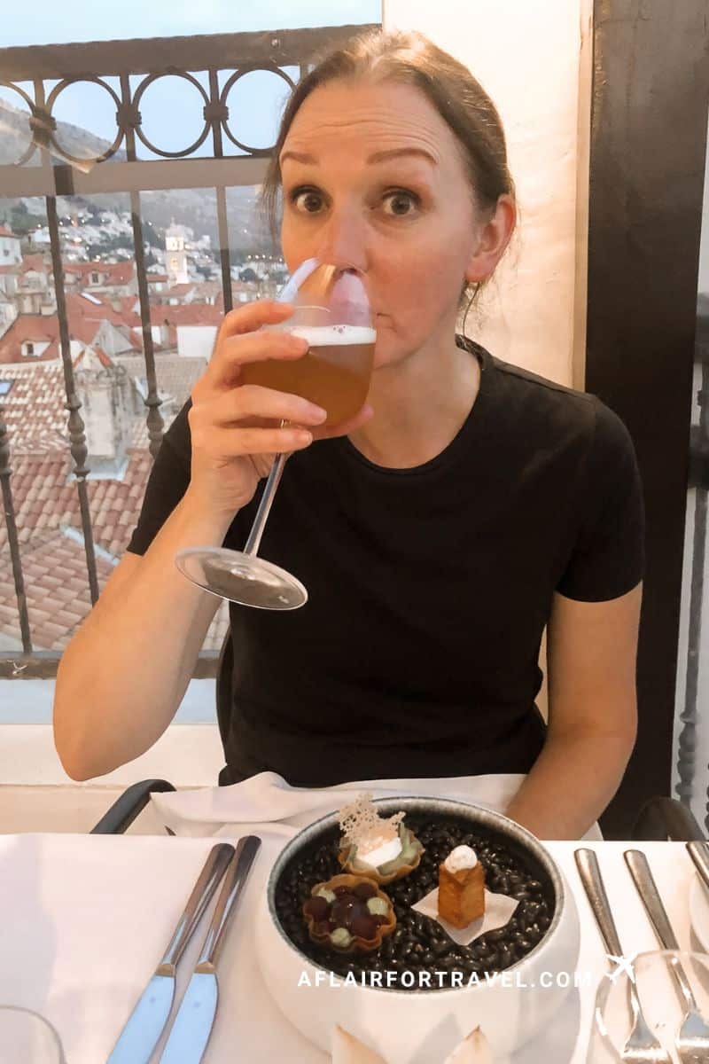 Woman enjoying a cocktail and petit fours at a rooftop restaurant overlooking Dubrovnik's Old Town rooftops