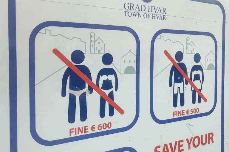 Sign in Hvar Town, Croatia warning visitors not to walk around town in swimwear, with fines of €500–€600 displayed for violations, an example of what not to do in Croatia.