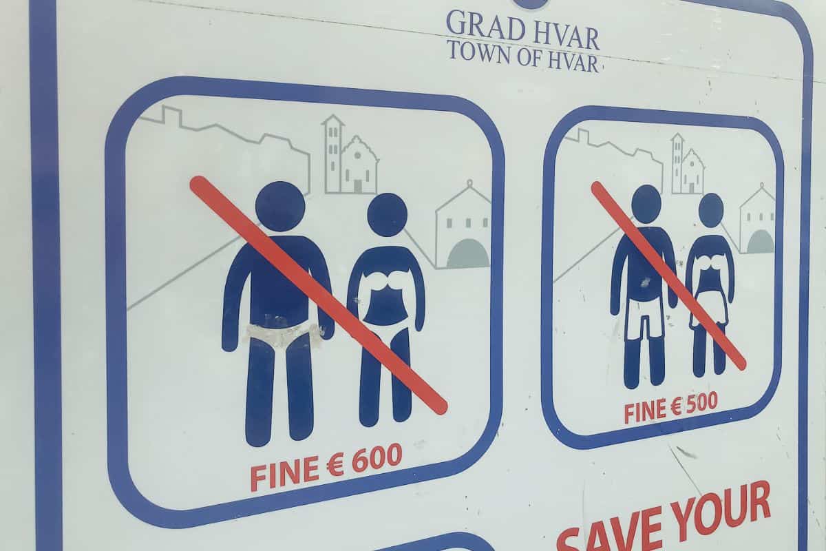 Sign in Hvar Town, Croatia warning visitors not to walk around town in swimwear, with fines of €500–€600 displayed for violations, an example of what not to do in Croatia.