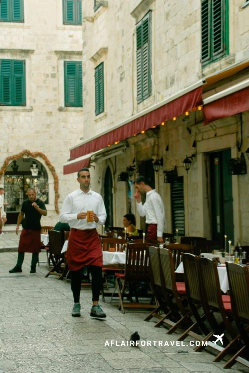 Waiters serving at a candlelit outdoor restaurant in Dubrovnik's Old Town, a reminder to tip and that not tipping is an example of what not to do in Croatia