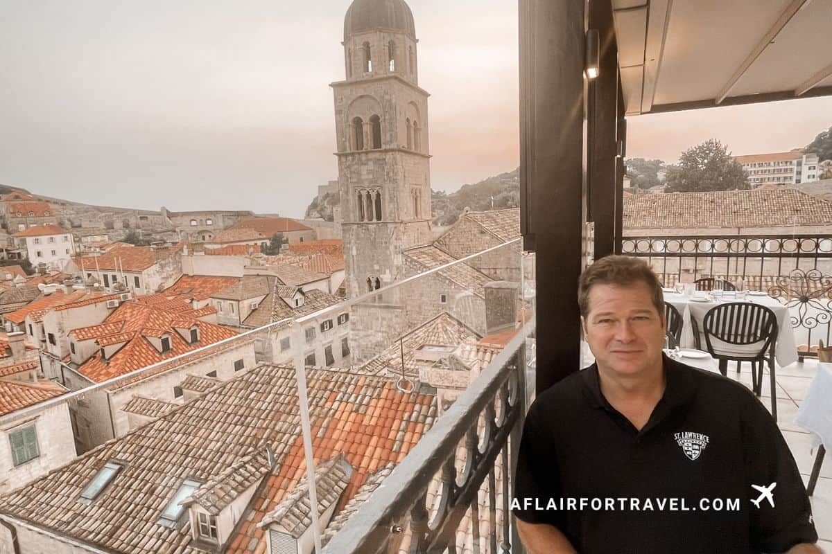 A guest on the rooftop terrace at Boutique Hotel Stari Grad Dubrovnik, with sweeping views across the terracotta rooftops of the old town and the Dominican Church bell tower at sunset.