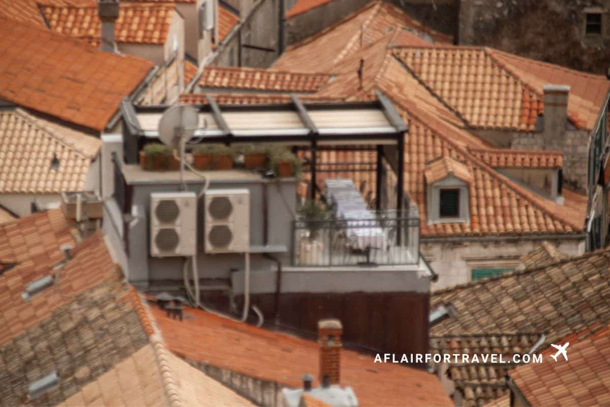 An aerial view of the Above 5 restaurant rooftop terrace at Boutique Hotel Stari Grad Dubrovnik, nestled among the terracotta rooftops of the old town, with a dining table set under a glass canopy.