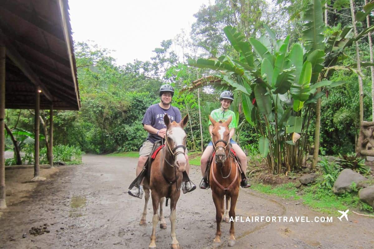 Father and daughter horseback riding through the rainforest