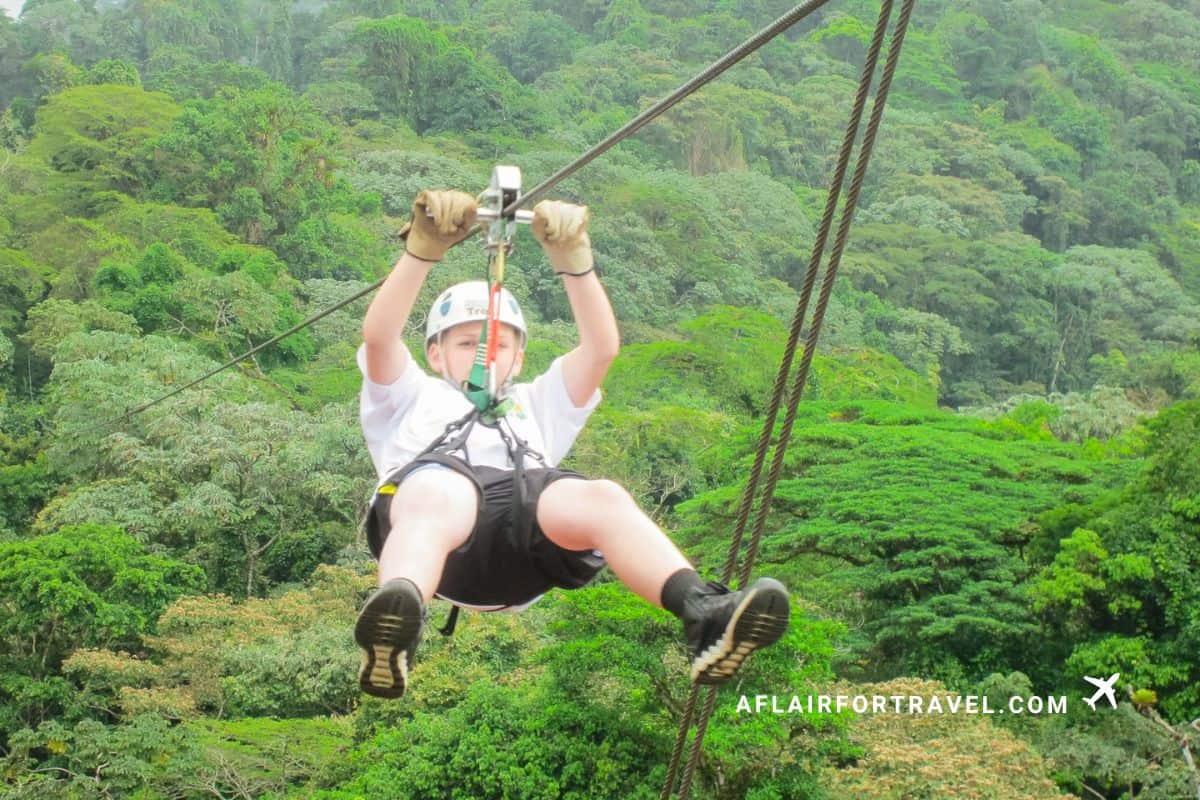 A boy soaring through the Arenal rainforest canopy on a zipline adventure, a must-do experiencen for a Costa Rica family itinerary