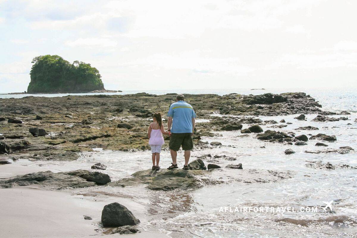 A father and daughter explore tide pools with an island in the distance during a trip to Costa Rica with kids