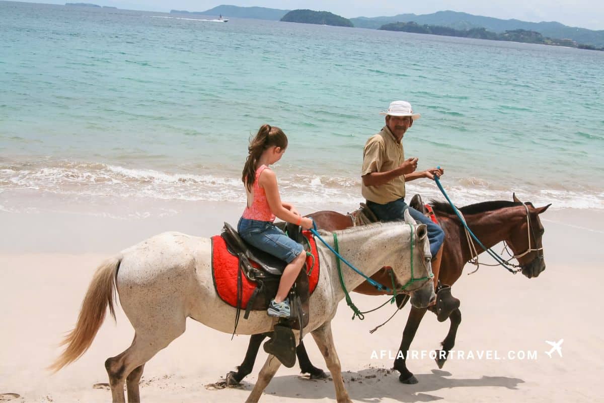 A girl horseback rides along the beach with a local guide during a trip to Costa Rica with kids
