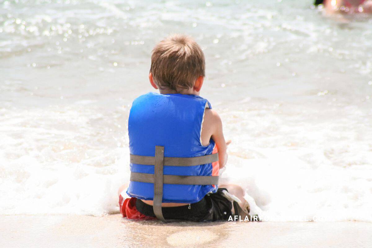 A young boy in a life vest sits at the edge of the surf in Costa Rica