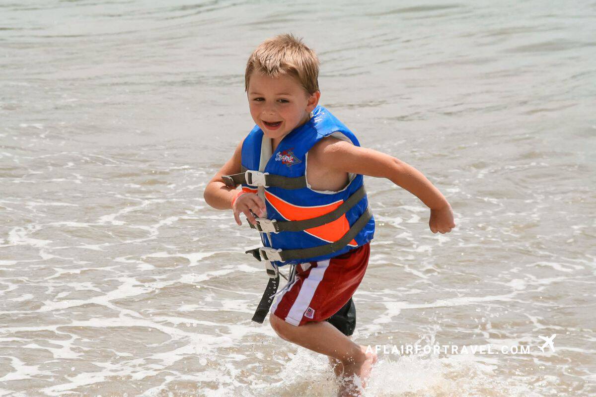 A young boy runs and laughs through the shallow waves in his life vest while in Costa Rica