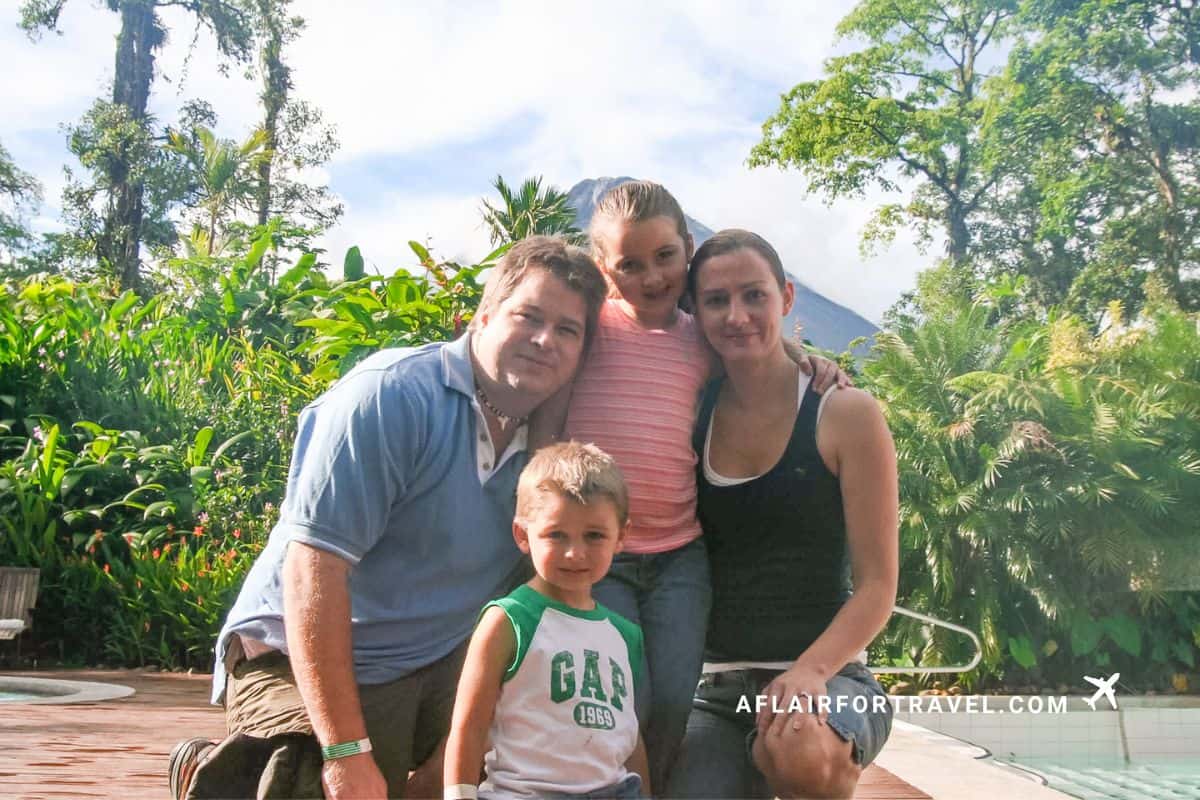 A family of four poses together with Arenal Volcano rising behind them during a family itinerary in Costa Rica