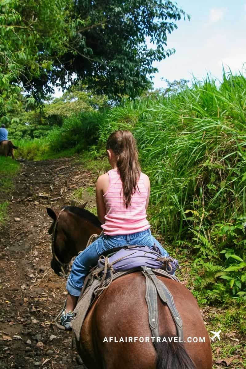 A girl rides horseback along a lush jungle trail in Costa Rica