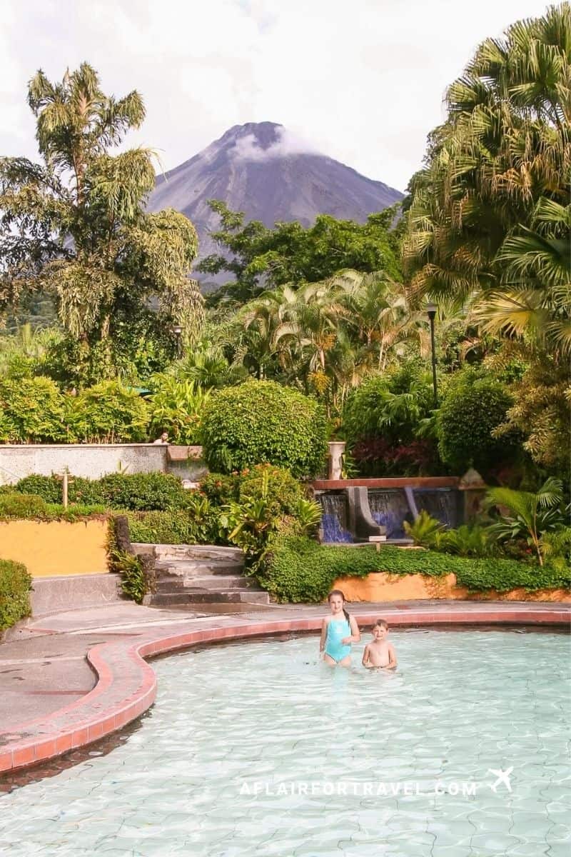 A young boy and girl enjoying a hot springs pool with Arenal Volcano in view during an itinerary in Costa Rica with kids