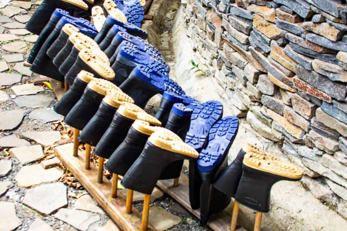 Rows of rubber rain boots drying upside down on wooden racks outside a Costa Rican rainforest lodge for the rainy weather which is what to expect in Monteverde, Costa Rica