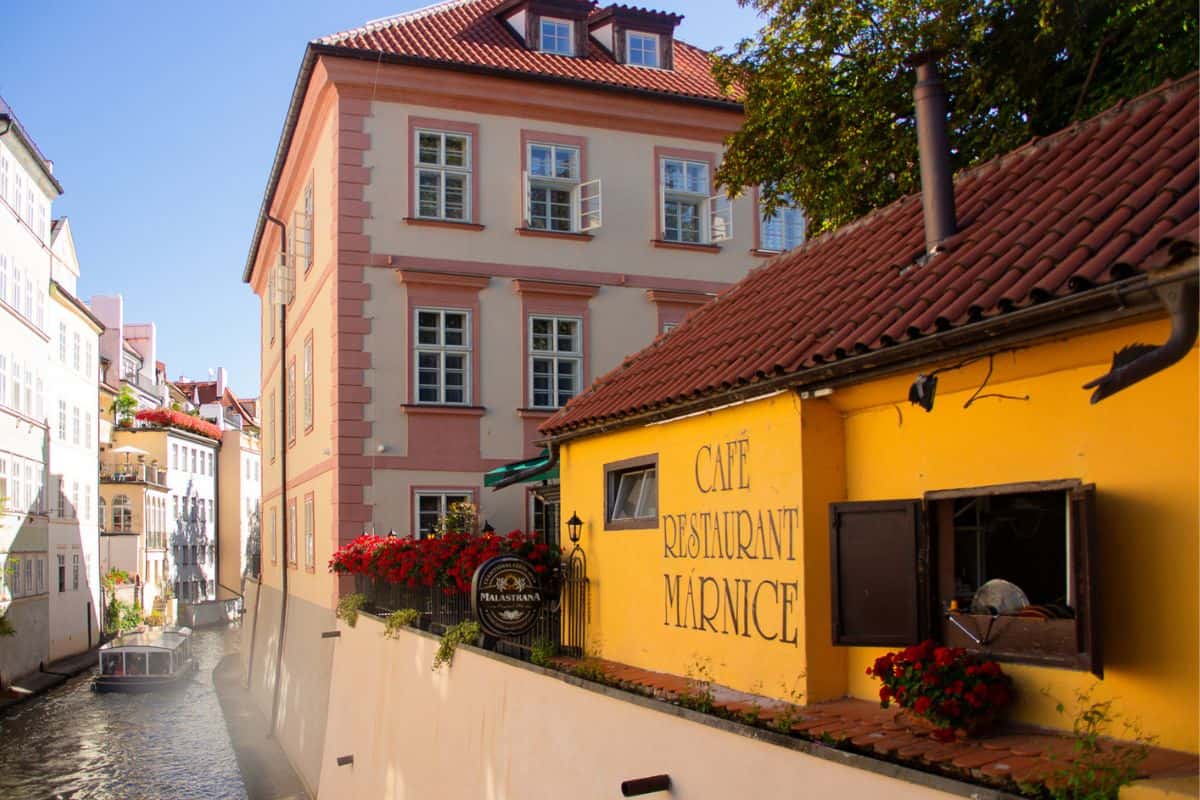 Colorful buildings and a charming café restaurant lining a quiet canal in Prague's Malá Strana, a picturesque stop in Prague