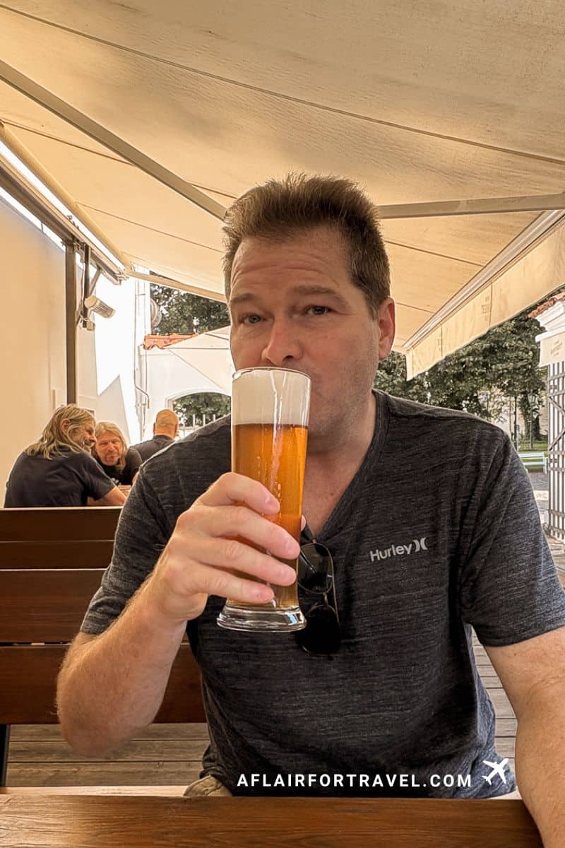 Man sipping a wheat beer at a wooden outdoor café table in Prague