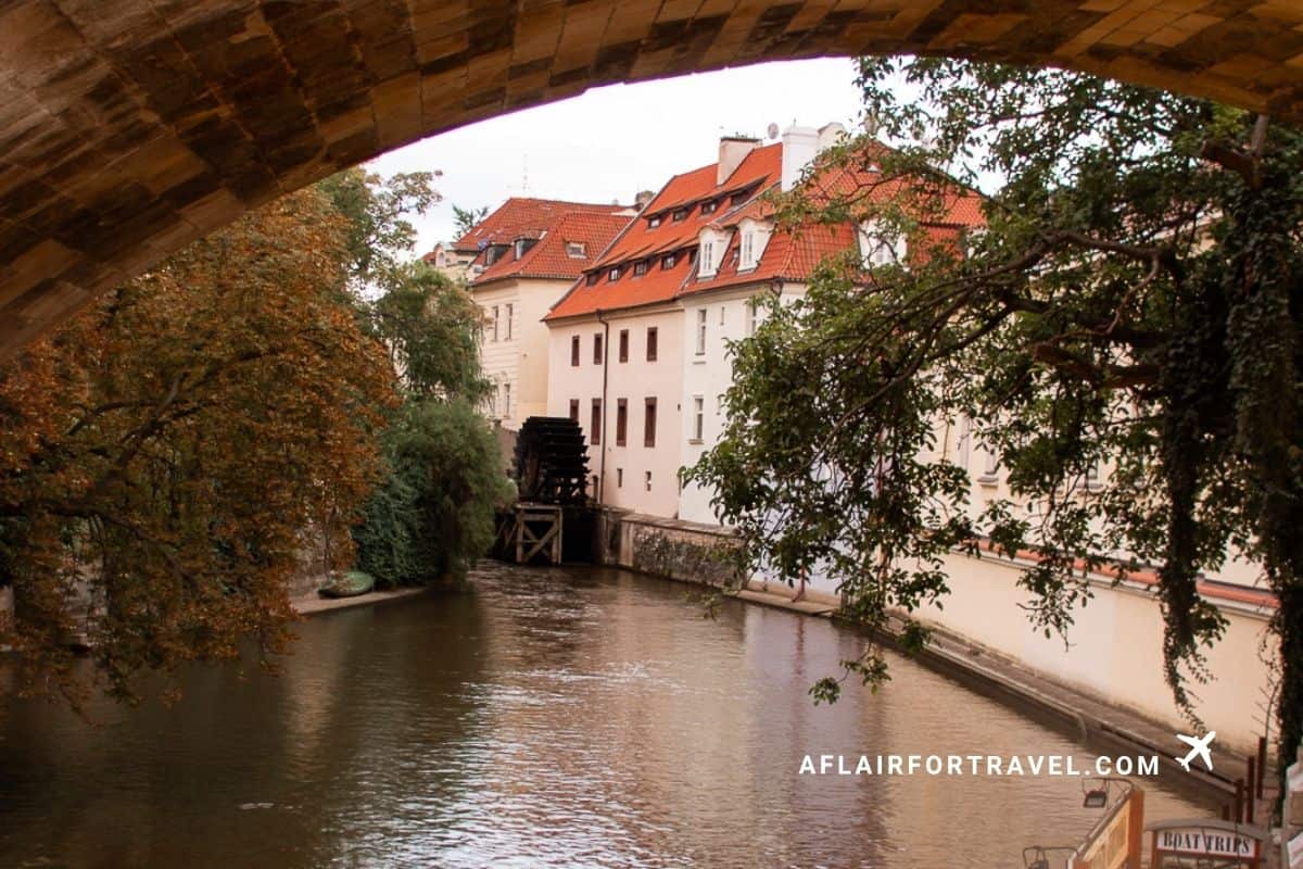 View through a stone bridge arch of the Čertovka canal, with its old wooden water wheel