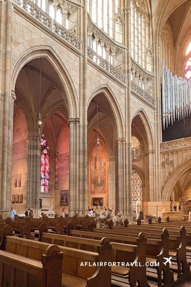 Gothic nave of St. Vitus Cathedral showing soaring stone arches, stained glass windows, and wooden pews