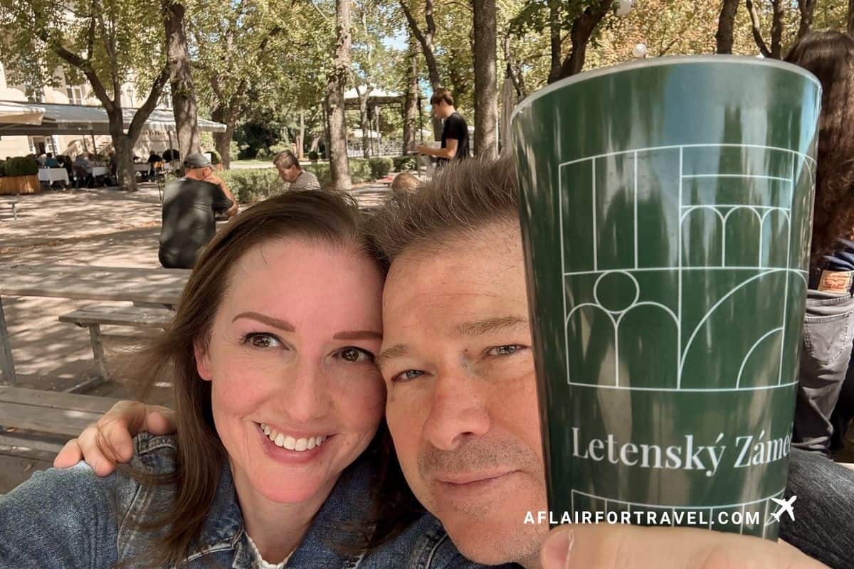 Couple holding a Letenský Zámeček beer cup in Letná Park, one of the Prague travel tips first-timers should know is that a returnable deposit is required for the cups.
