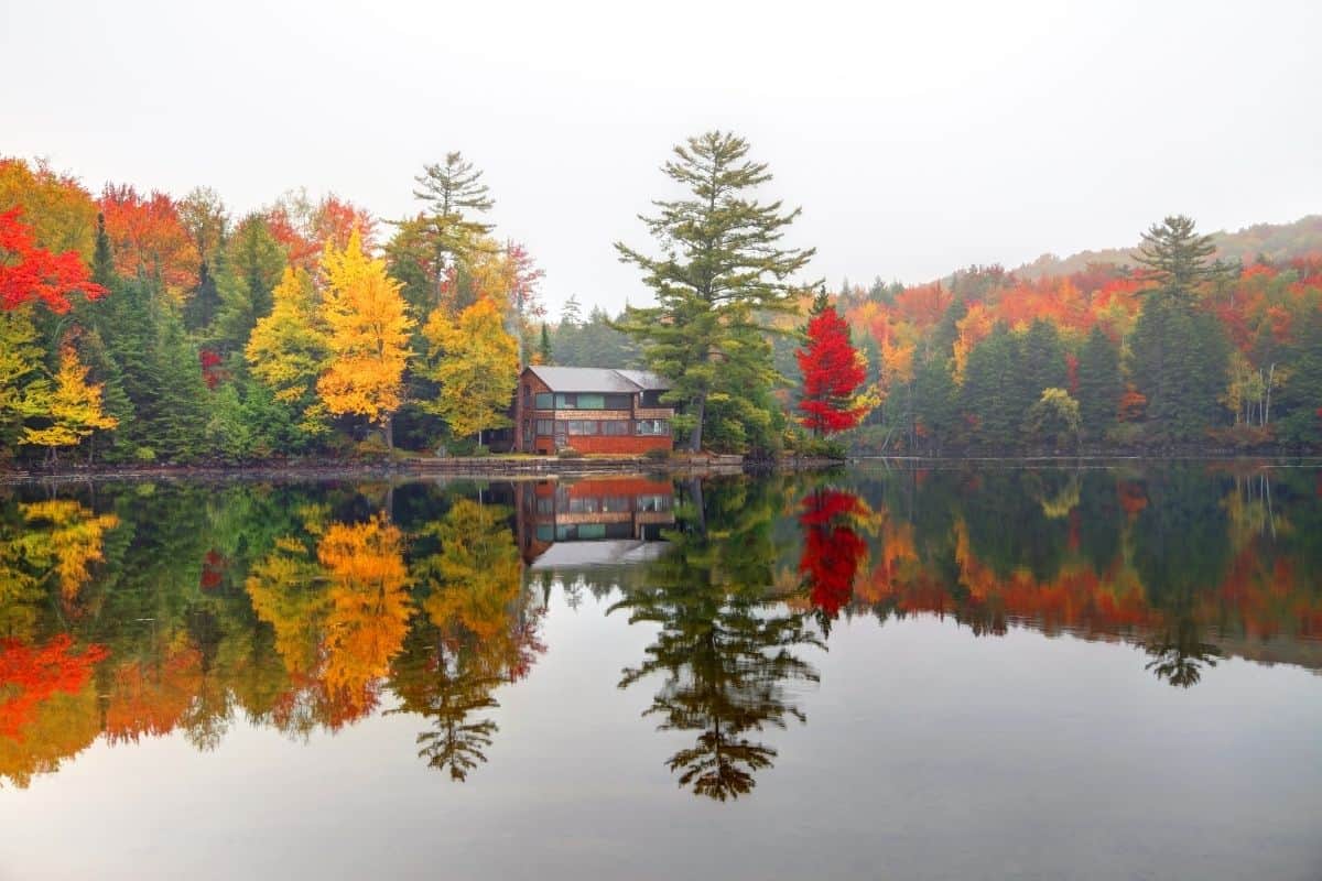 Lakeside cabin in the Great North Woods in New Hampshire in the fall, surrounded by red and gold foliage reflected in still water