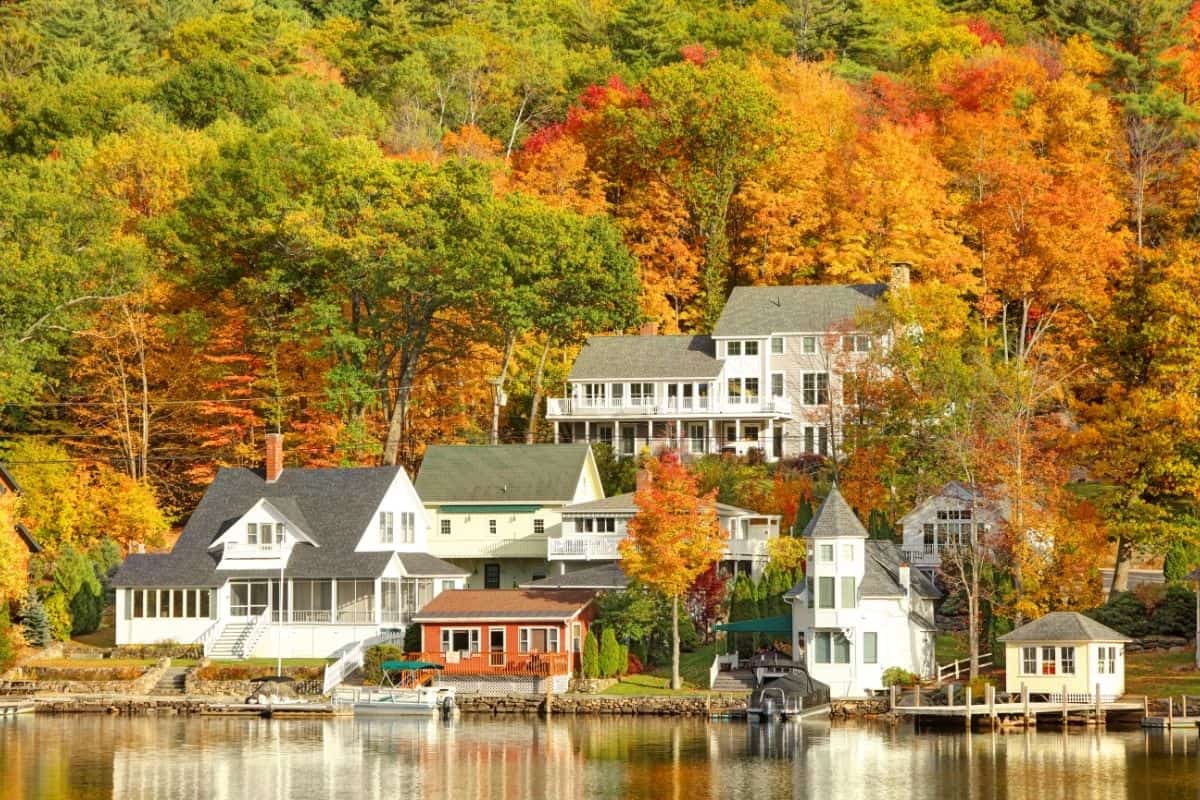 Lakefront homes on Lake Sunapee nestled into a hillside of red, orange, and green autumn trees