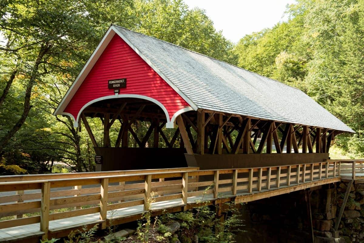 Red covered bridge in the Flume Gorge with a wooden pedestrian walkway crossing a forested river
