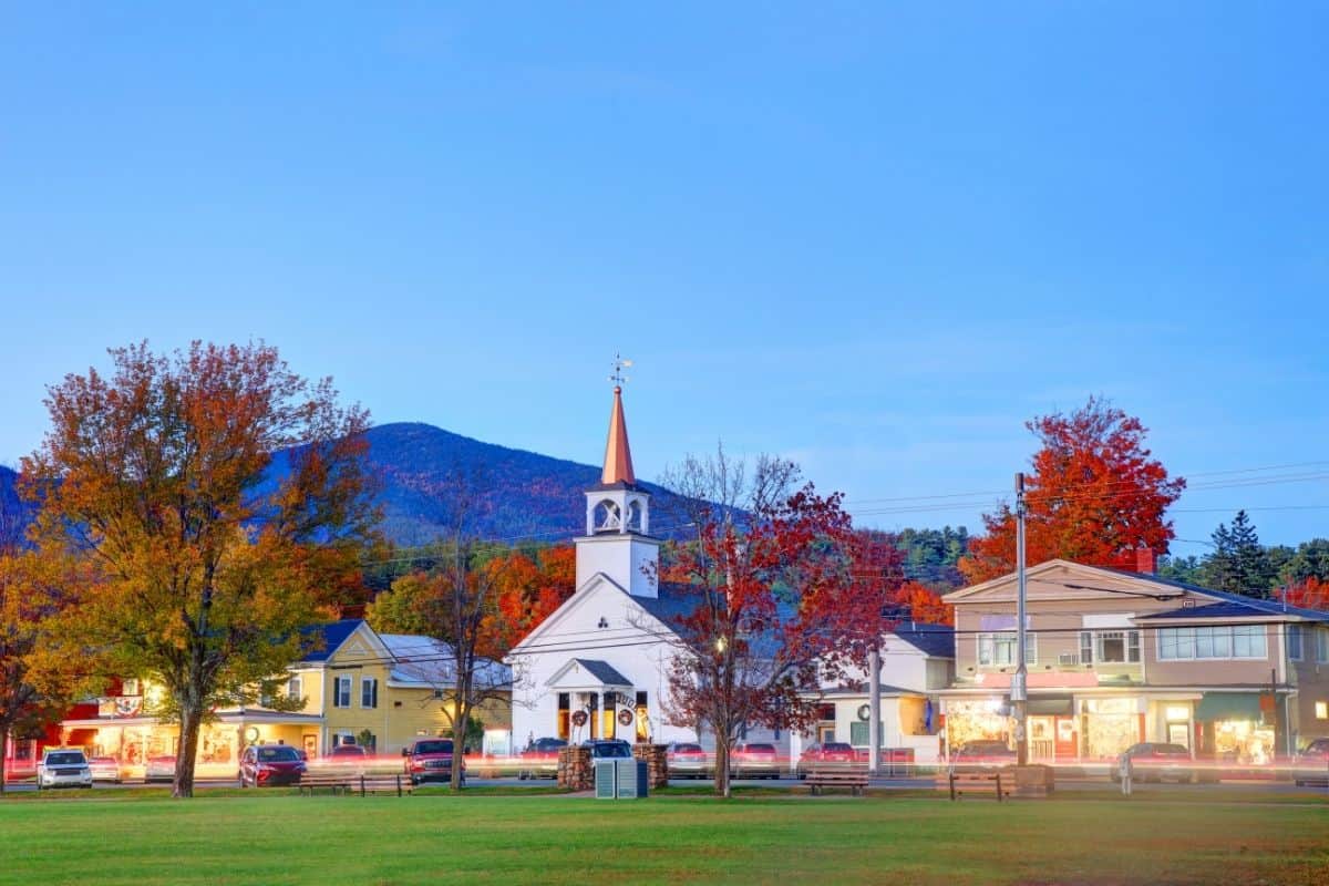 North Conway, New Hampshire at dusk with a church steeple and fall-colored trees against the mountains