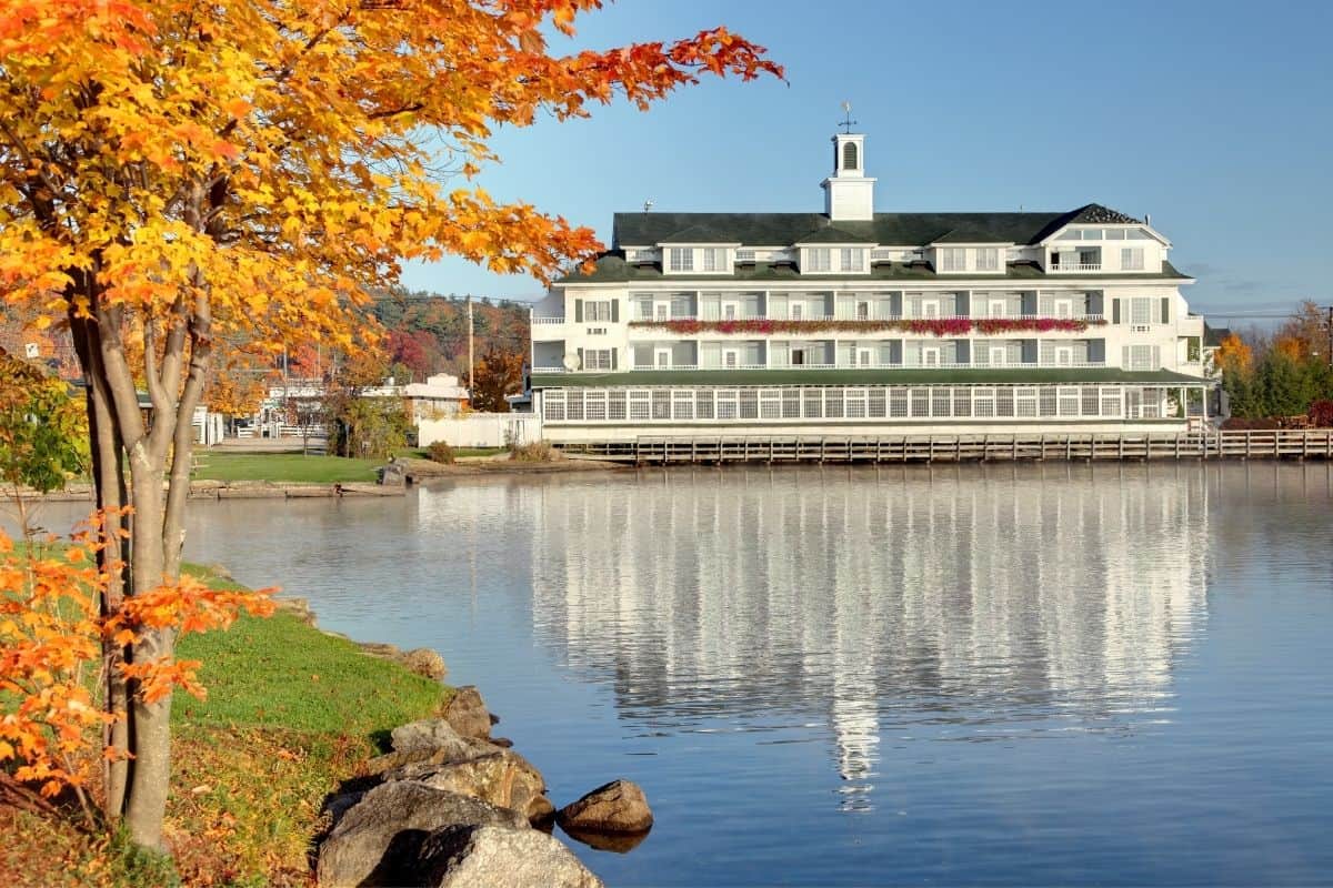White colonial-style building on Lake Winnipesaukee framed by a bright orange maple tree