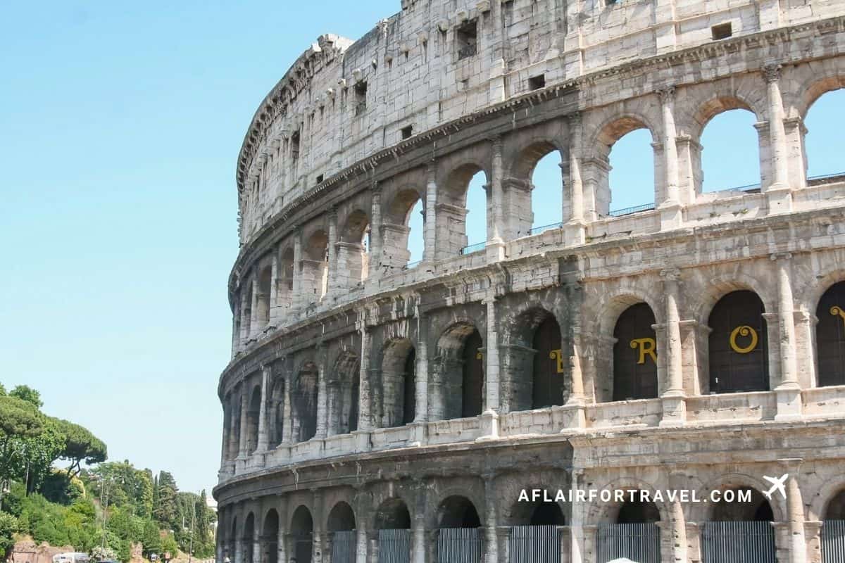 The Colosseum's ancient arched exterior under a clear blue sky in Rome, a must-see for any first-time trip to Europe