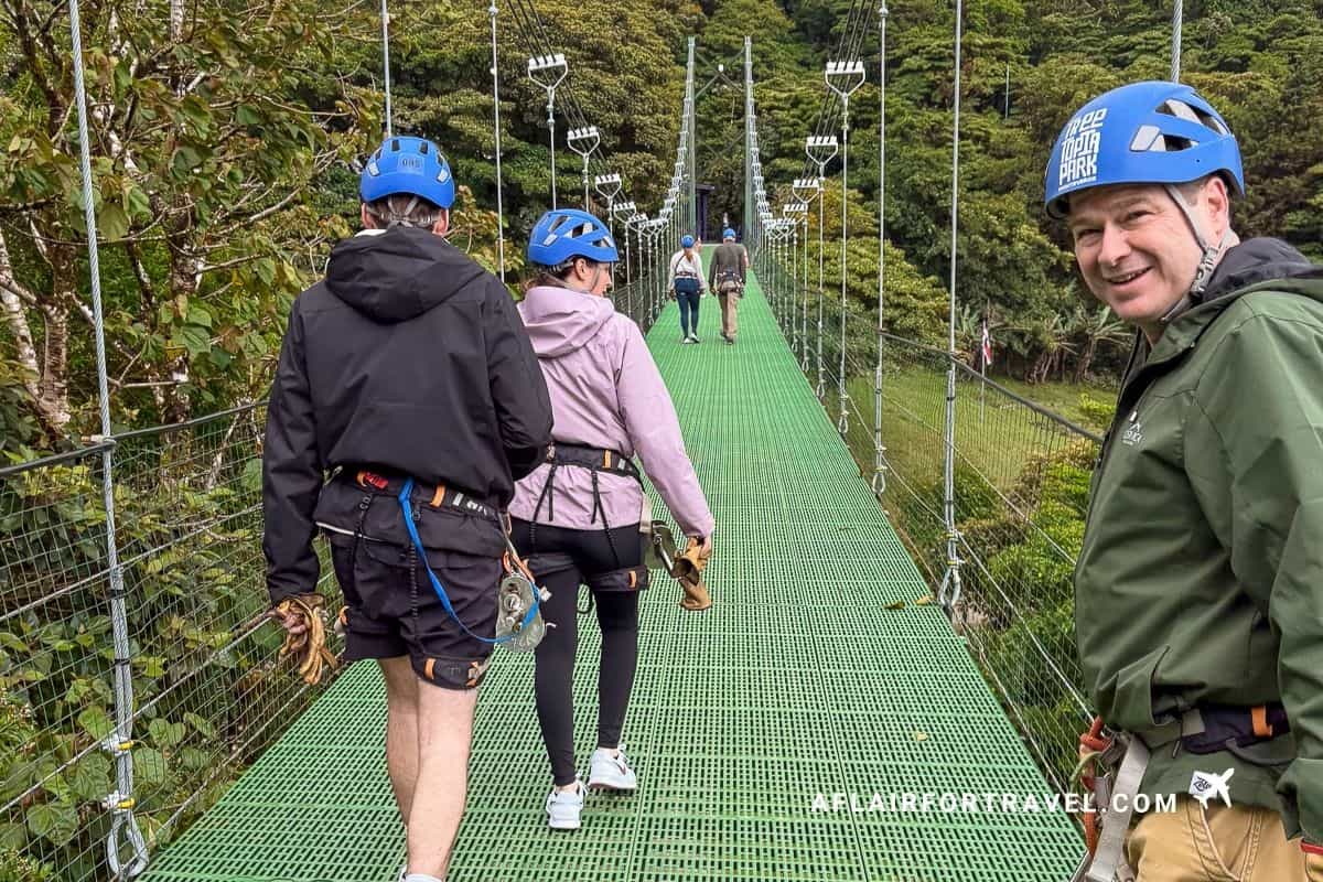 Group crossing a green hanging bridge in helmets and harnesses, part of a canopy tour in Monteverde, Costa Rica