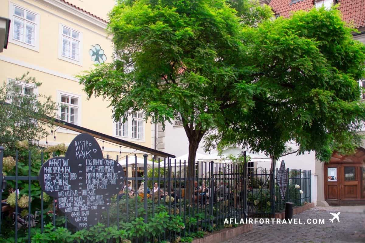 Bistro Monk's outdoor courtyard seating under a shade tree in Prague; one of the top Prague travel tips is to skip the hotel breakfast and eat at cafes.