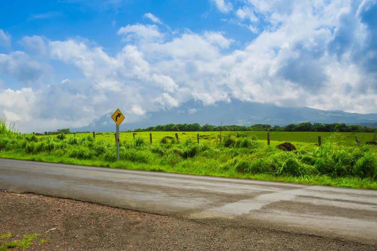 Curve warning road sign along a rural highway in Costa Rica, with volcanic peaks in the background