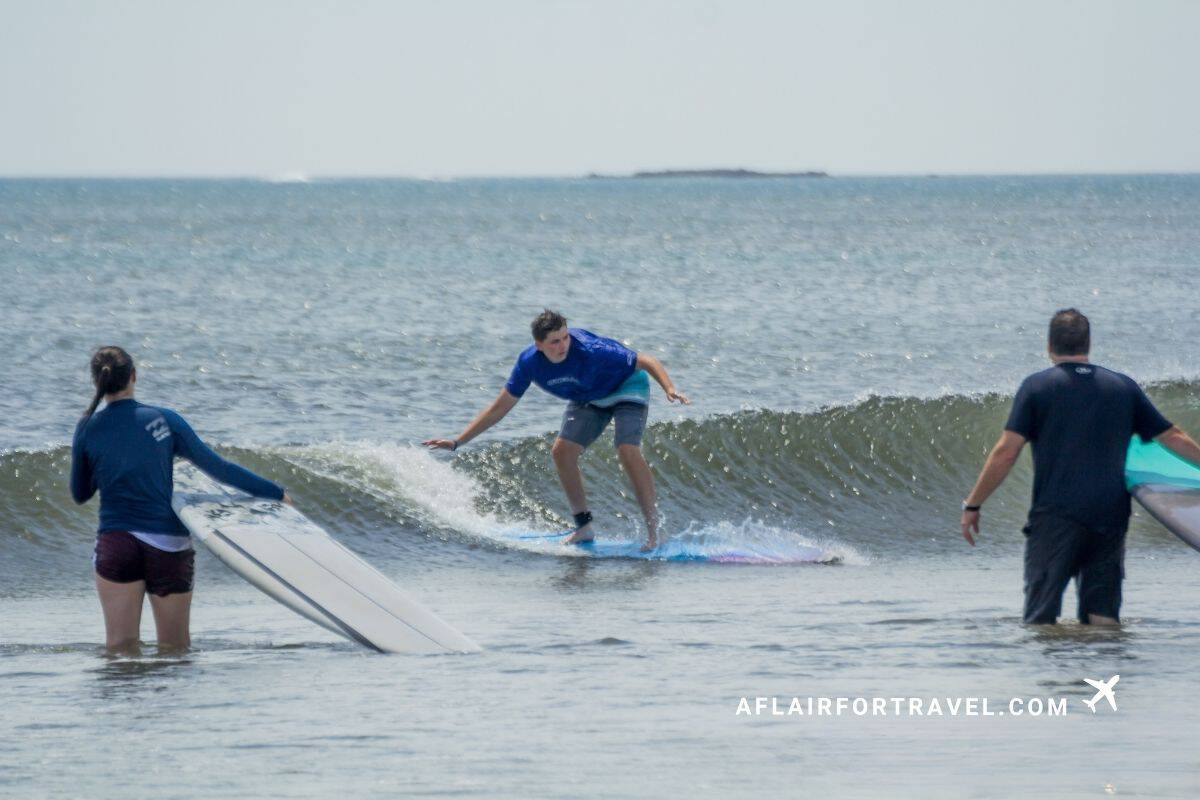 Teenage boy surfing in Tamarindo while his sister and father look on
