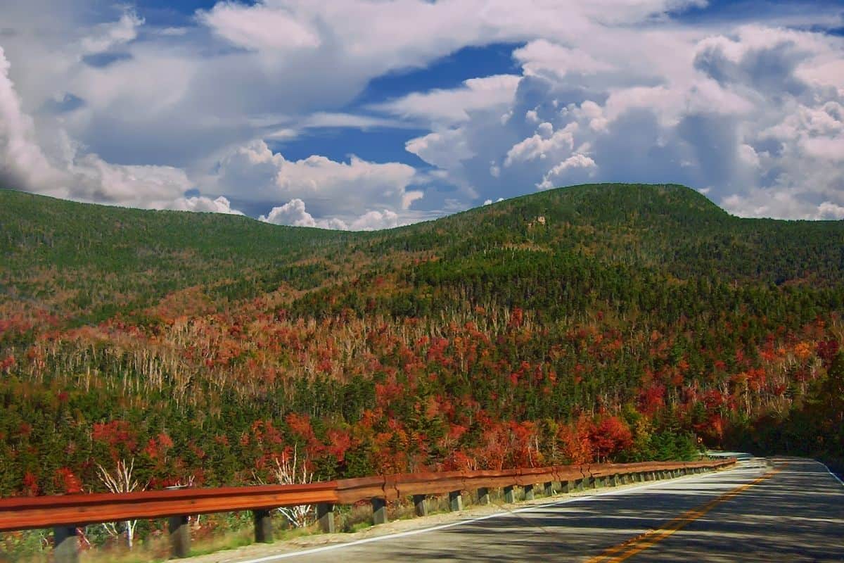 Winding Kancamagus Highway bordered by fall foliage under a cloudy sky