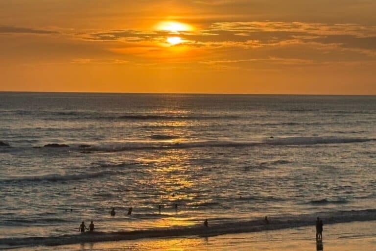 Sun setting over the water at a Costa Rica beach with a bright orange sky and people watching from the shore