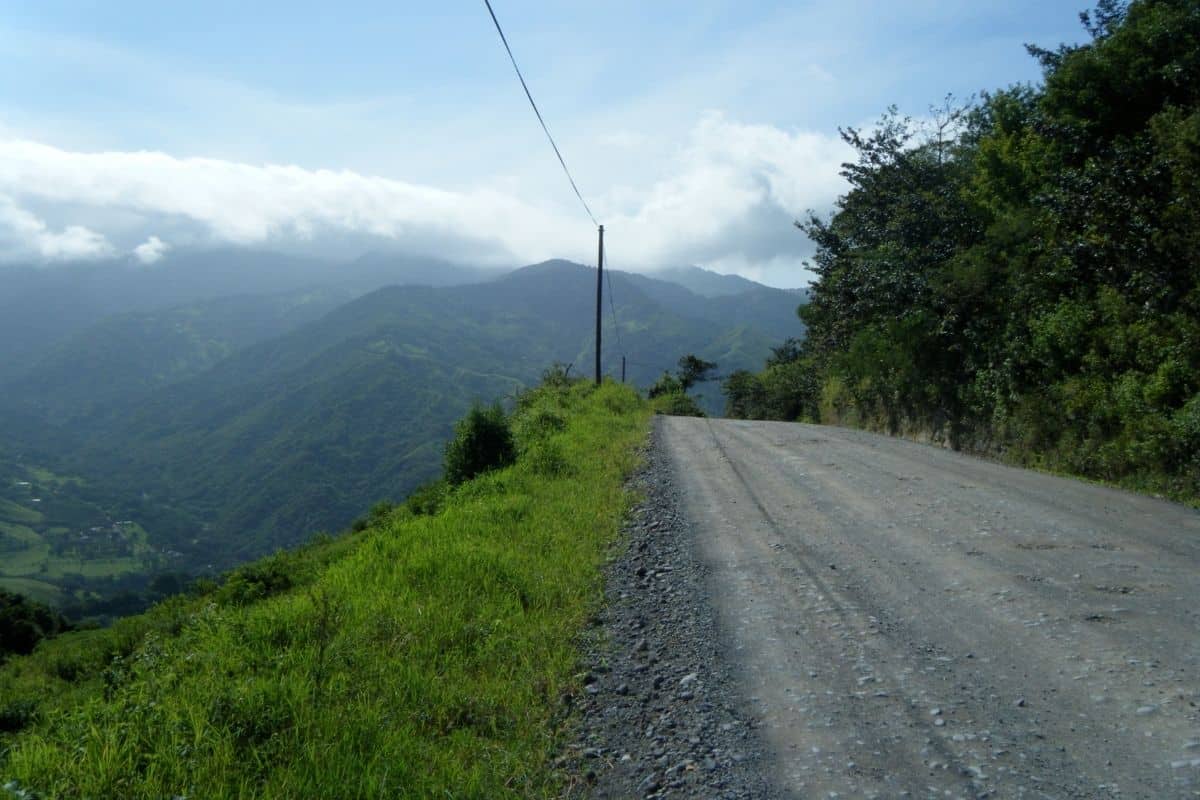 Gravel mountain road overlooking a lush green valley, a scenic stretch for driving in Costa Rica