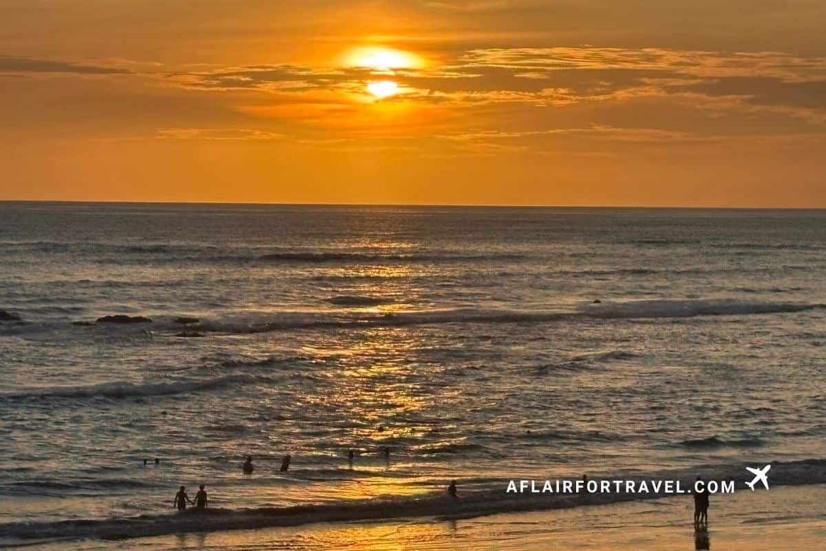 Sun setting over the water at a Costa Rica beach with a bright orange sky and people watching from the shore