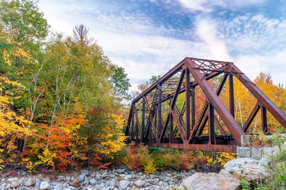 Rusty steel truss bridge surrounded by autumn foliage in New Hampshire