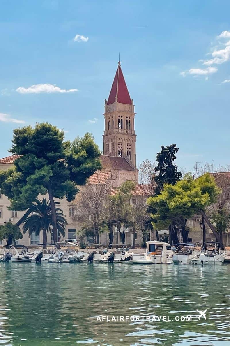 Red-roofed bell tower overlooking a harbor filled with boats in Trogir, Croatia