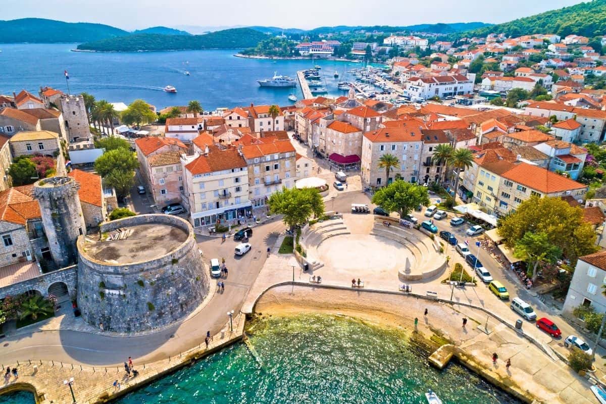 Aerial view of Korčula's harbor, fortress tower, and red-roofed old town