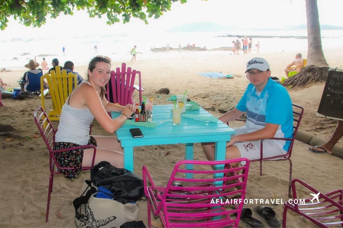 Teenage girl and boy sitting at a colorful table at a beachside restaurant in Costa Rica