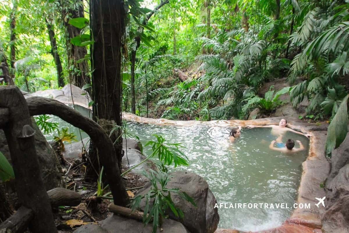 Three family members sitting in a hot spring pool surrounded by rainforest foliage in Costa Rica