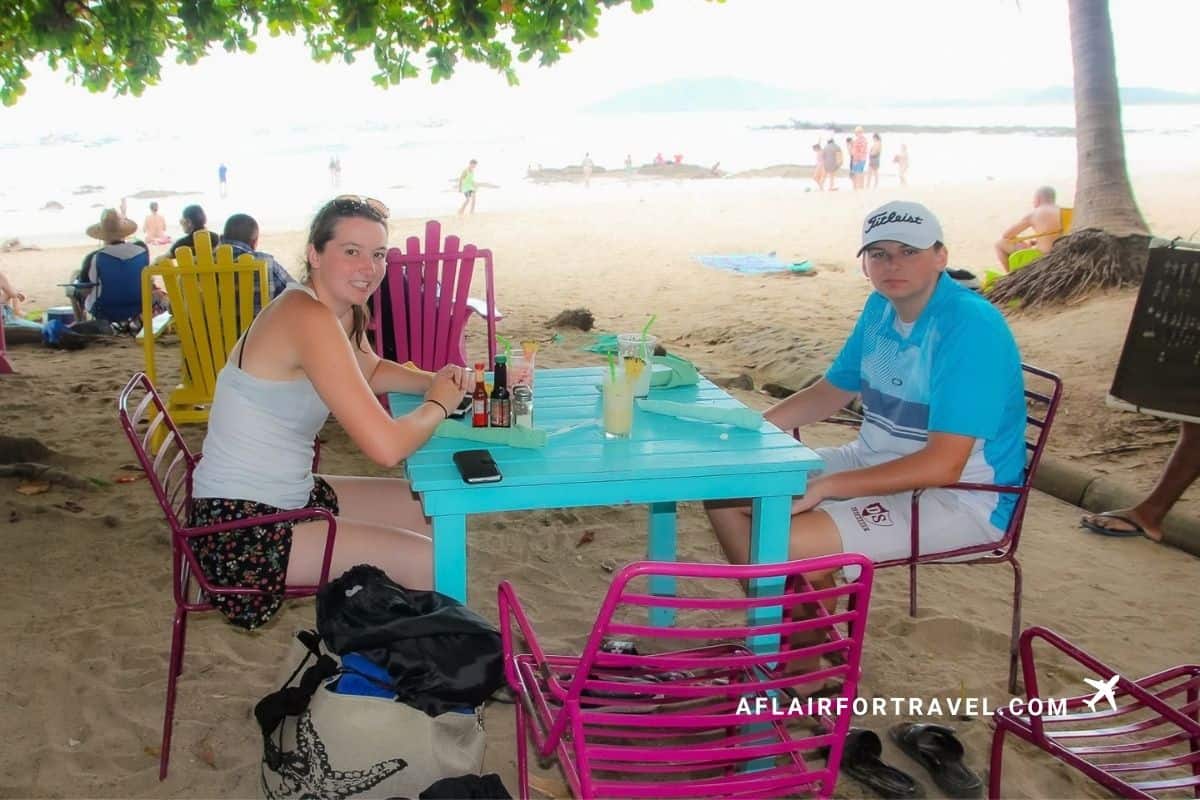 A brother and sister sitting at a colorful beachside table setting on Tamarindo Beach