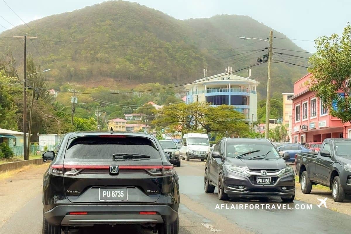 Cars navigating a narrow, rain-slicked road through a St. Lucia town
